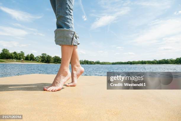 barefoot woman standing tiptoe on pier at lake - hochgekrempelte hose stock-fotos und bilder