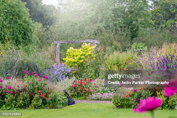 beautiful english cottage garden in soft summer sunshine with a rustic wooden arch garden feature - domestic garden stock pictures, royalty-free photos & images