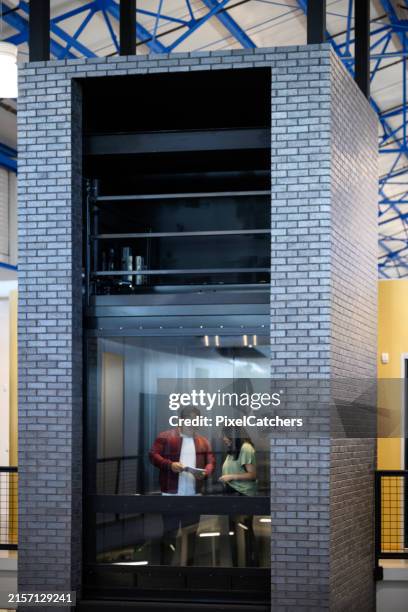 des collègues discutent de documents dans un ascenseur en verre au travail - ascenseur verre photos et images de collection