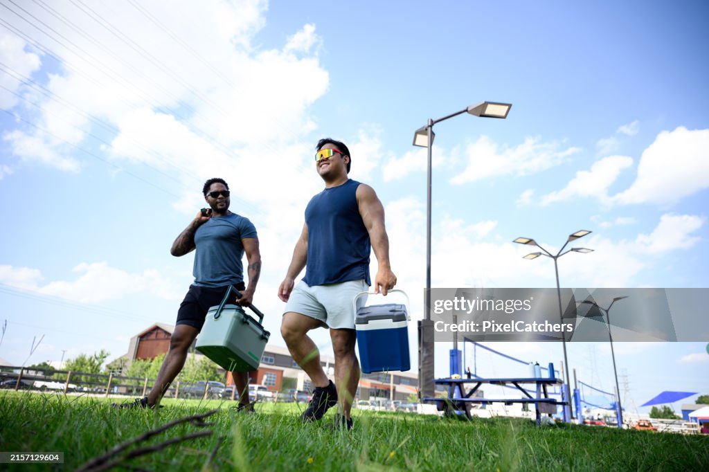 Men walking and talking together outside by sports grounds carrying cooler box