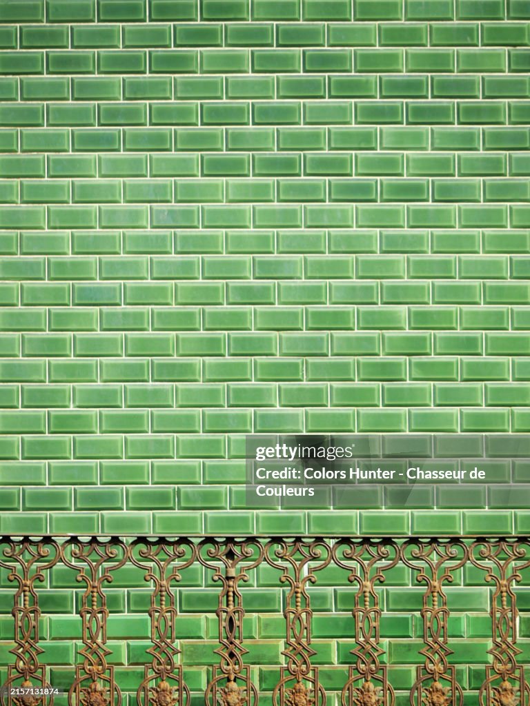 Close-up of a wall covered with green tiles with an old metal railing in Porto, Portugal. Sunlight. Natural colors and patina.