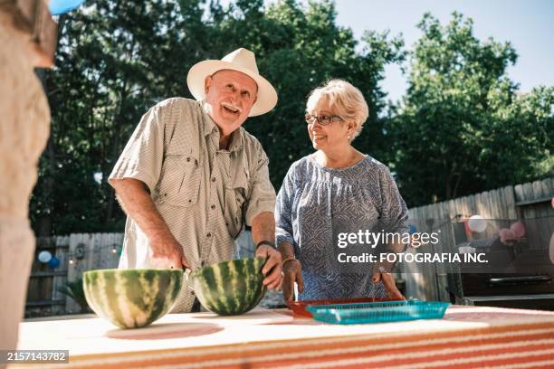 senior latino couple serving watermelon at the backyard party - southern usa stock pictures, royalty-free photos & images