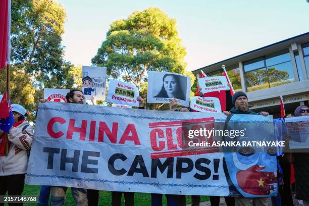 Uyghur and counter-China demonstrators hold a banner and placards as they await the arrival of China's Premier Li Qiang at the Adelaide Zoo in...