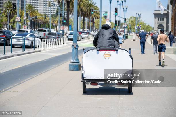 Pedicab driver on a busy Embarcadero sidewalk near the Ferry Building on a sunny day, San Francisco, California, June 7, 2024.