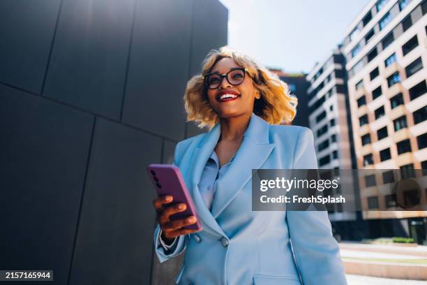 selbstbewusste geschäftsfrau, die mit dem smartphone im freien spazieren geht - blauer anzug stock-fotos und bilder