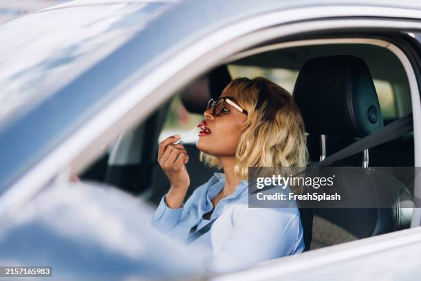 woman applying lipstick while sitting inside car - lippenstift stockfoto's en -beelden
