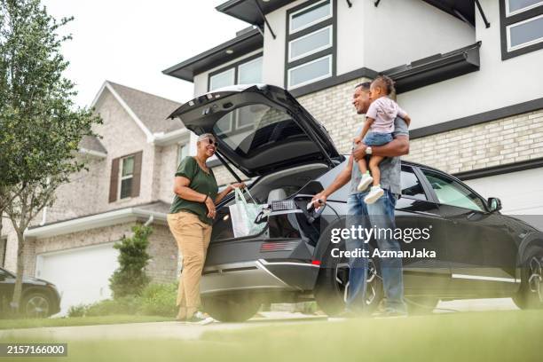 multiethnic grandparents unload their ev while charging - auto interieur stockfoto's en -beelden