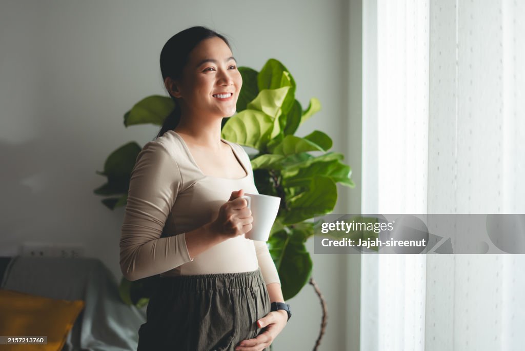 Asian pregnant woman happy relax time with hot drink in living room at home.