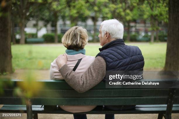 a senior couple embracing on a public bench in a park - troisième âge photos et images de collection