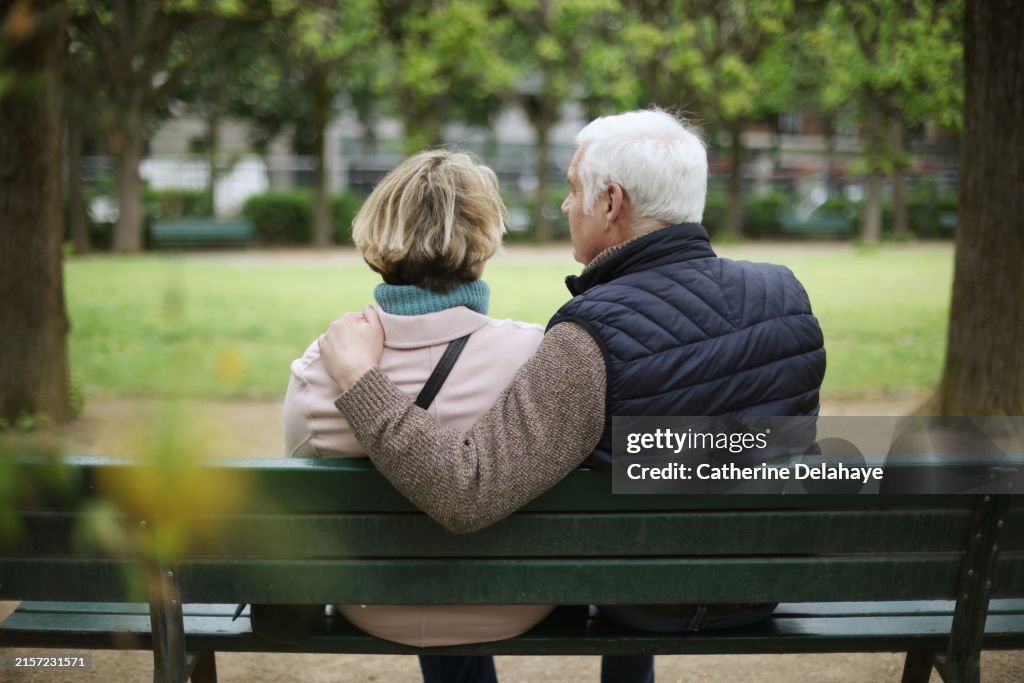A senior couple embracing on a public bench in a park