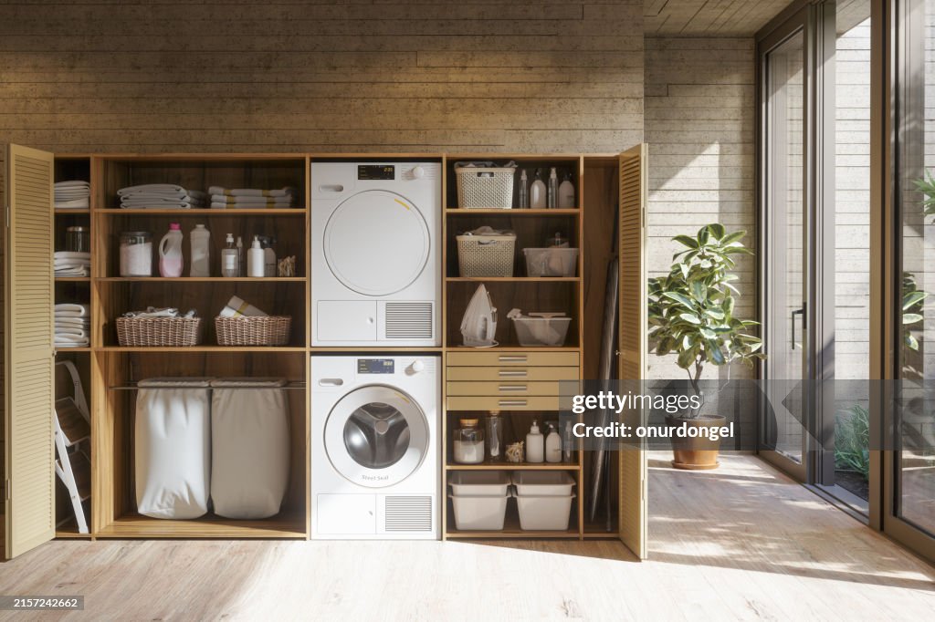 Moderne Waschküche mit Waschmaschine, Trockner, Wäschekorb und gefalteten Handtüchern im Schrank