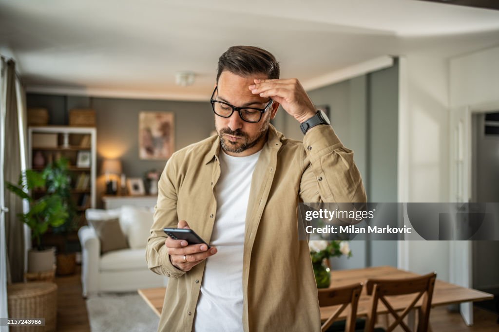 A young man is feeling depressed and thinking about the bad news he is reading online through his smartphone