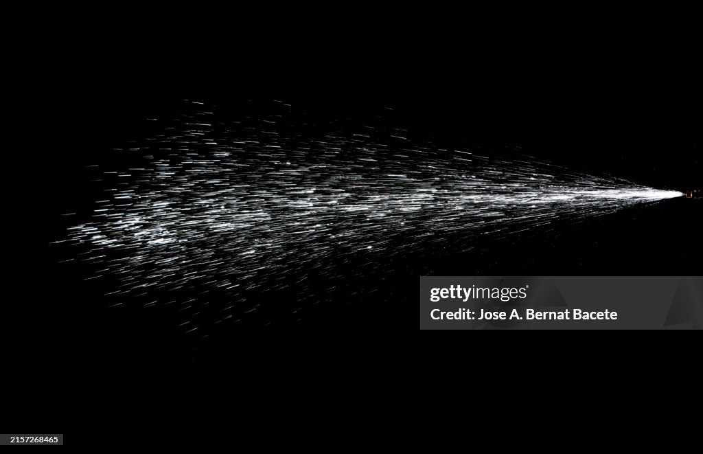 Jet of moving pressurized water drops on a black background.