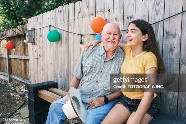 latino grandfather and his granddaughter enjoying shade at the backyard party - grandfather granddaughter stock pictures, royalty-free photos & images