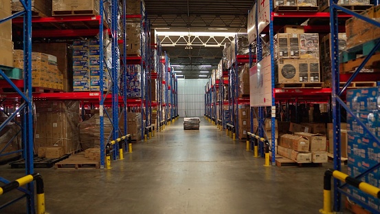 Distribution warehouse - forward view in modern warehouse full of shelves ready to be delivered of large factory. Storage room with racks arranged in a row. Boxes and packages stacking in shipping room. Racks full of packages, boxes, pallets, crates. No p