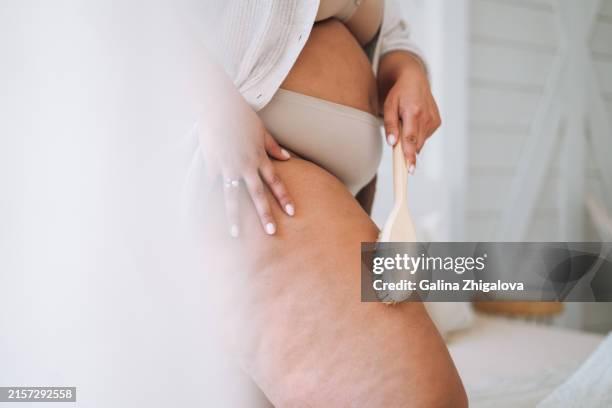 crop photo of young plus size woman in underwear doing body massage with dry wooden brush in bedroom at home - cellulite stock pictures, royalty-free photos & images