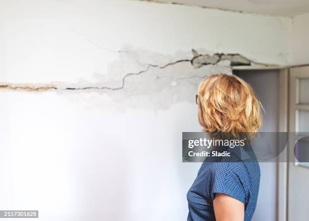 mujer mirando una pared dañada tras el terremoto - terremoto fotografías e imágenes de stock