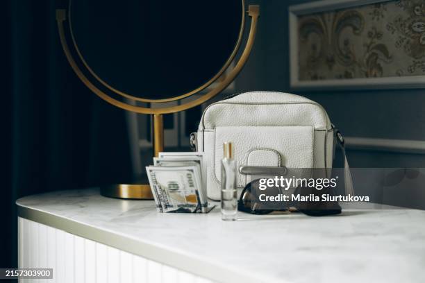 stylish white handbag, sunglasses, perfume, and cash on a marble vanity with a round mirror. - sac à main bigarré photos et images de collection