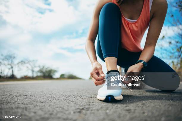 une jeune coureuse est dehors le matin, se préparant à faire son jogging. on la voit se pencher, attacher ses lacets, s’assurer que ses chaussures de course sont bien attachées avant de commencer sa course - attacher photos et images de collection