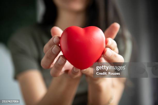 the woman is holding a red heart - cholesterol stockfoto's en -beelden