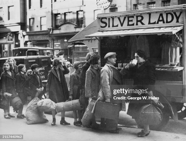Civilians in one of London's air raid damaged areas queuing around the Silver Lady Fund mobile canteen to receive warm food and drink before entering...