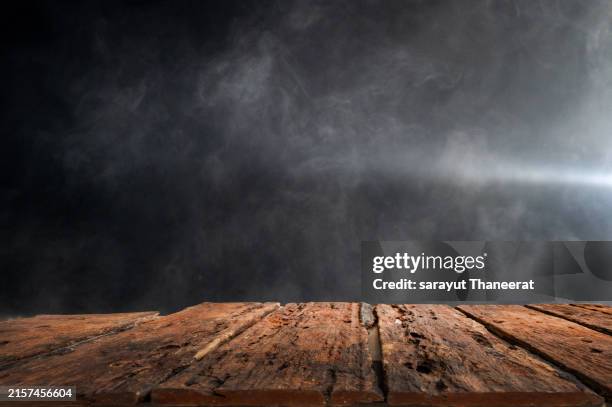 empty old wooden table with smoke float up on dark background on a black background, an empty wooden table with smoke floats up. empty space for displaying your products, with a smoke float up on a dark background. space available for displaying your prod - holztisch stock-fotos und bilder