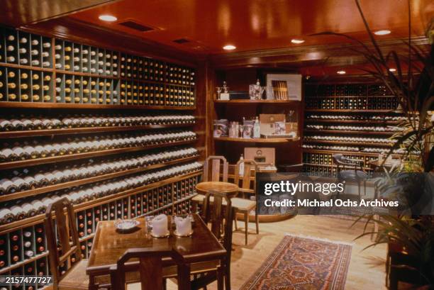 Racks of wine bottles beyond tables and chairs in Hamilton's, a cigar bar in Beverly Hills, California, circa 1990. The bar, to which Hamilton lent...