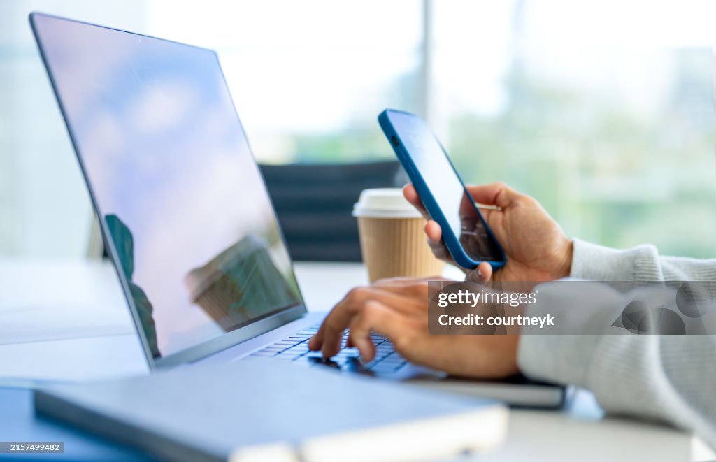 Close up of a Businessman working on a laptop computer and holding and looking at a mobile phone in the office.