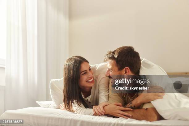 happy couple talking during morning in a bed. - dekbed stockfoto's en -beelden