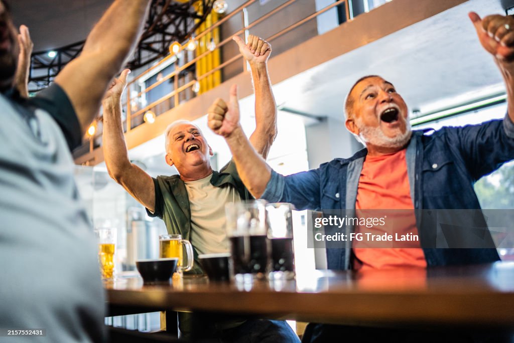 Senior men celebrating a goal in soccer game at bar