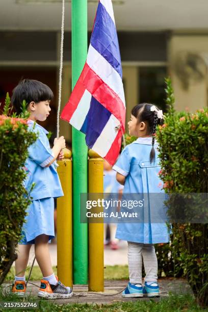 kindergarten students participating in flag raising ceremony outdoors - flagpole stock pictures, royalty-free photos & images