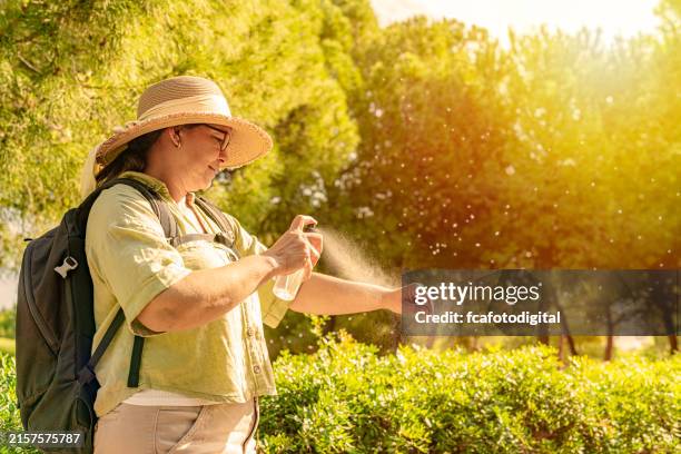 mujer aplicándose repelente de insectos en el brazo en un parque público - mosquito fotografías e imágenes de stock