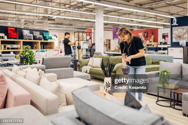 two smiling salespeople in a department store decorate a section with sofa beds and living room sets on display - loja de móveis imagens e fotografias de stock