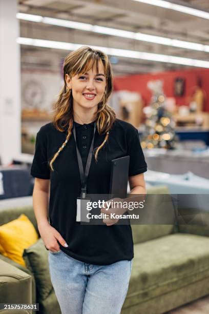 a smiling saleswoman looks directly into the camera while standing in a department store - loja de móveis imagens e fotografias de stock