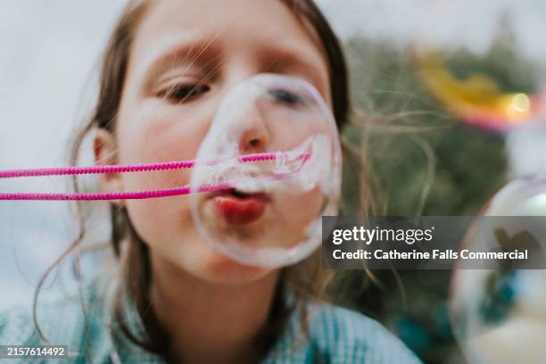 a child holds a bubble wand, and blows bubbles towards the camera - innocenza foto e immagini stock