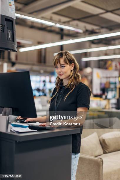 a female worker in a furniture store is focused on using a computer - retail store computer stock pictures, royalty-free photos & images