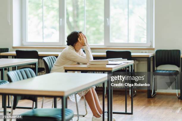 exam failure: sad woman with her face in her hands sits at desk. - distraught stock pictures, royalty-free photos & images