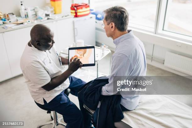high angle view of doctor discussing male reproductive system with patient on digital tablet while sitting in medical ro - prostate-cancer stock pictures, royalty-free photos & images