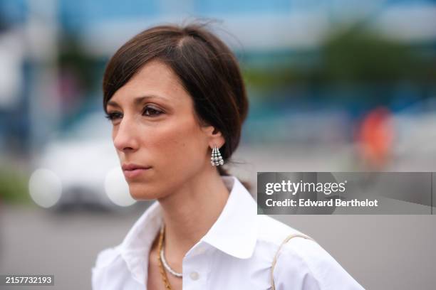 Guest wears silver earrings, gold chained necklace, silver necklace, an open oversized white button up shirt, outside MSGM, during the Milan Fashion...