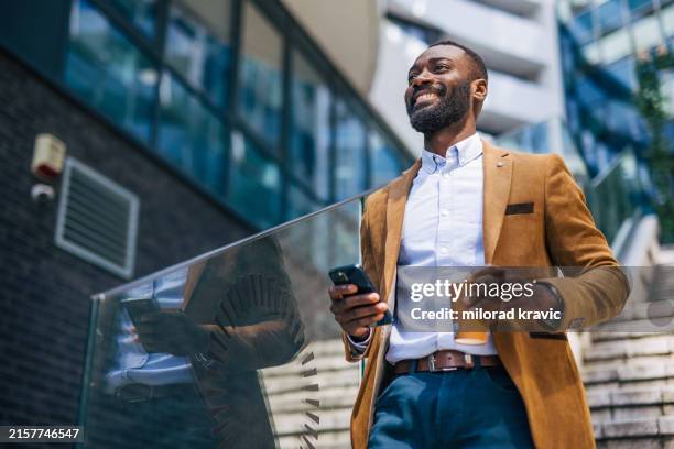 ein erwachsener, gutaussehender schwarzer geschäftsmann außerhalb eines unternehmens, der das telefon benutzt - afrikanischer abstammung stock-fotos und bilder