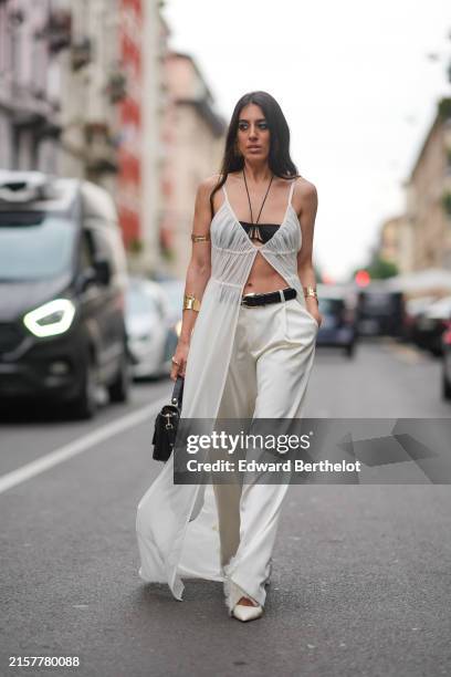 Nil Ninat wears white sheer long dress open midway, black top, black belt, white loose pants, white heels, gold necklace with black string, gold...