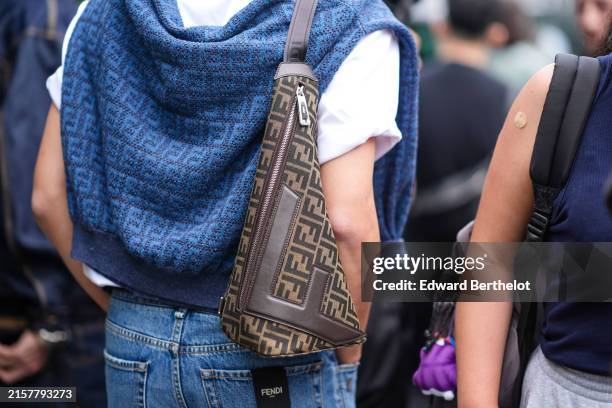 Guest wears white shirt, blue Fendi sweater on shoulders, Fendi brown brown bag, baggy jeans, outside Fendi during the Milan Fashion Week Menswear...