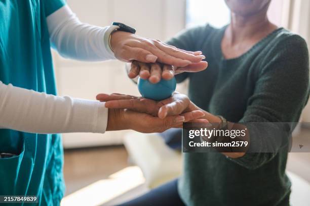 female young nurse assisting senior patient in squeezing hand therapy balls at a rehabilitation center - human spine stock pictures, royalty-free photos & images