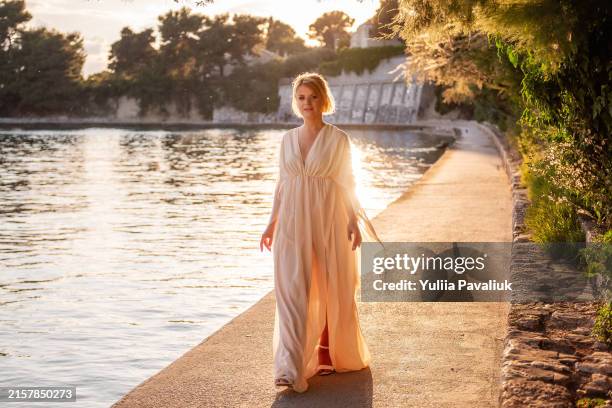 woman in flowing dress walking by water at sunset - beautiful woman walking flowing dress stock pictures, royalty-free photos & images