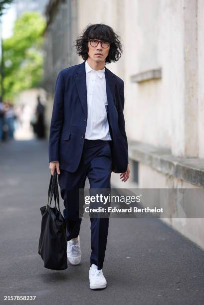 Guest wears brown glasses, white button up shirt, navy blazer jacket, navy pants, white sneakers, black bag, outside Prada, during the Milan Fashion...