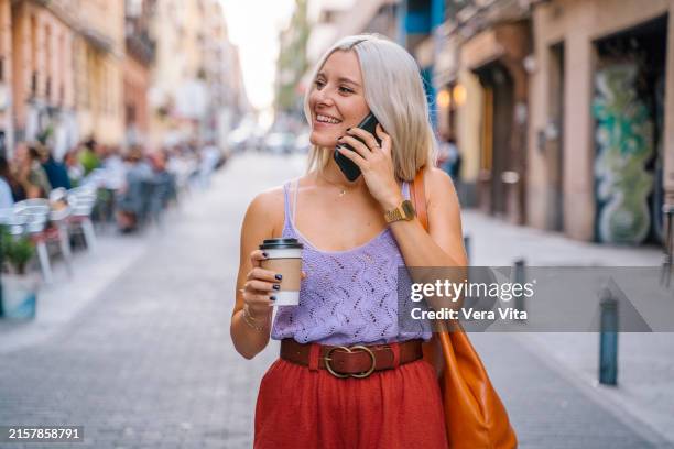 portrait of blonde woman walking on the street drinking take away coffee - takeaway coffee stock pictures, royalty-free photos & images