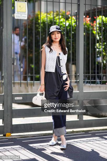 Guest wears a black baseball hat, pearl necklaces, gray spotted vest, black dress with flower detail, navy straight legged denim jean pants cropped,...