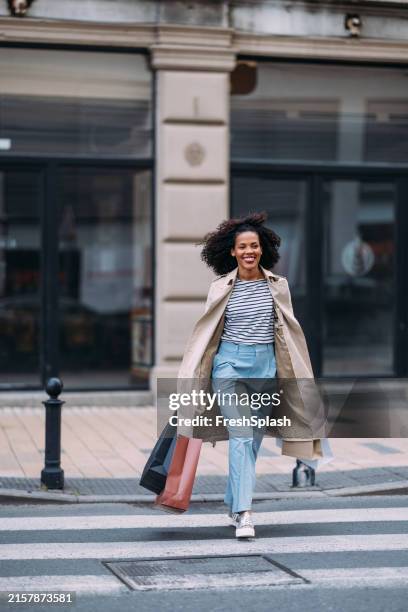 femme heureuse marchant dans la rue de la ville avec des sacs à provisions - traverser photos et images de collection
