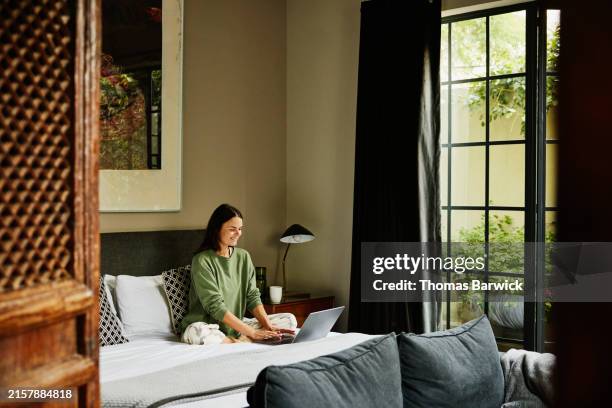 wide shot woman working on laptop on bed in luxury boutique hotel - hotel suite stock pictures, royalty-free photos & images