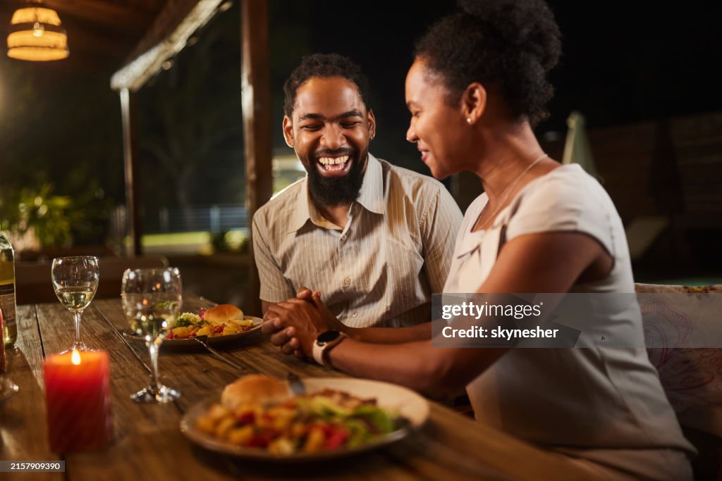 Alegre casal negro conversando durante o jantar em um pátio.